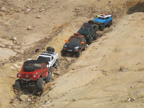 1988 Ford Bronco - Several remote control off-road vehicles navigate a rocky, dusty trail in a line.
