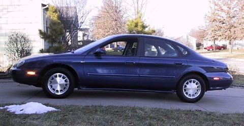 1996 Ford Taurus - Side view of a dark blue 1996 Ford Taurus sedan parked on a driveway.