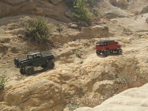 1988 Ford Bronco - Two remote-controlled off-road vehicles navigate a , rocky terrain under a bright sky.