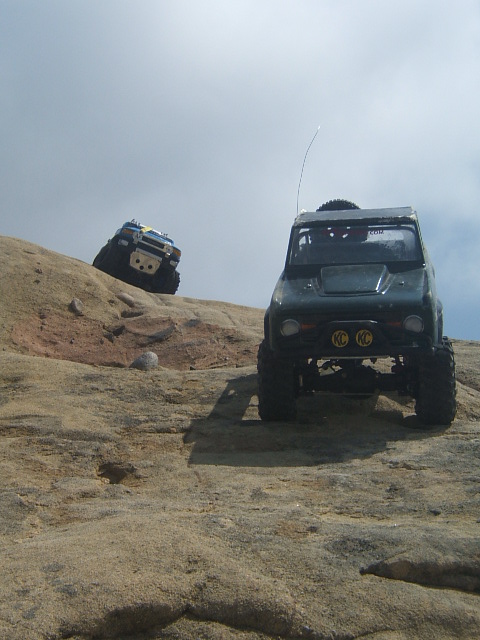 1988 Ford Bronco - Two RC off-road vehicles navigate a rocky landscape under a cloudy sky.