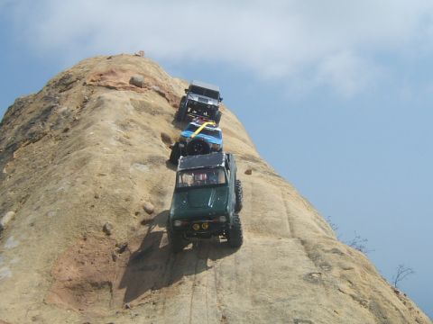 1988 Ford Bronco - Multiple off-road vehicles navigate a challenging rocky incline on a sunny day.