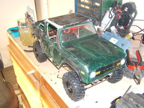 1988 Ford Bronco - A green RC crawler model resembling an early Ford Bronco sits on a cluttered workbench.