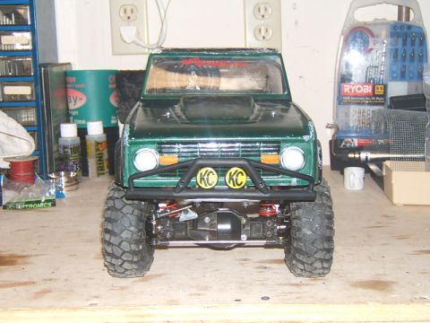 1988 Ford Bronco - This green RC crawler truck features KC lights and aggressive off-road tires, viewed from the front.