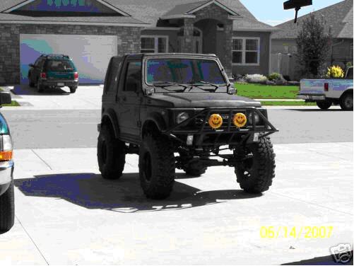 Black lifted Suzuki Samurai with tube bumper and amber lights parked in a driveway