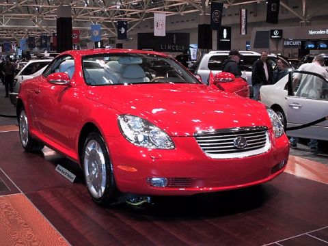 1996 Ford Taurus - A red coupe is displayed indoors with other vehicles and signage in the background.