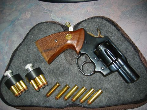 1996 Ford Bronco - A black revolver with wooden grips is displayed with speedloaders and loose cartridges on a gray fabric surface.