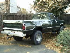1974 Dodge 1500 - A dark green Dodge pickup truck is parked outdoors with dry leaves on the ground.