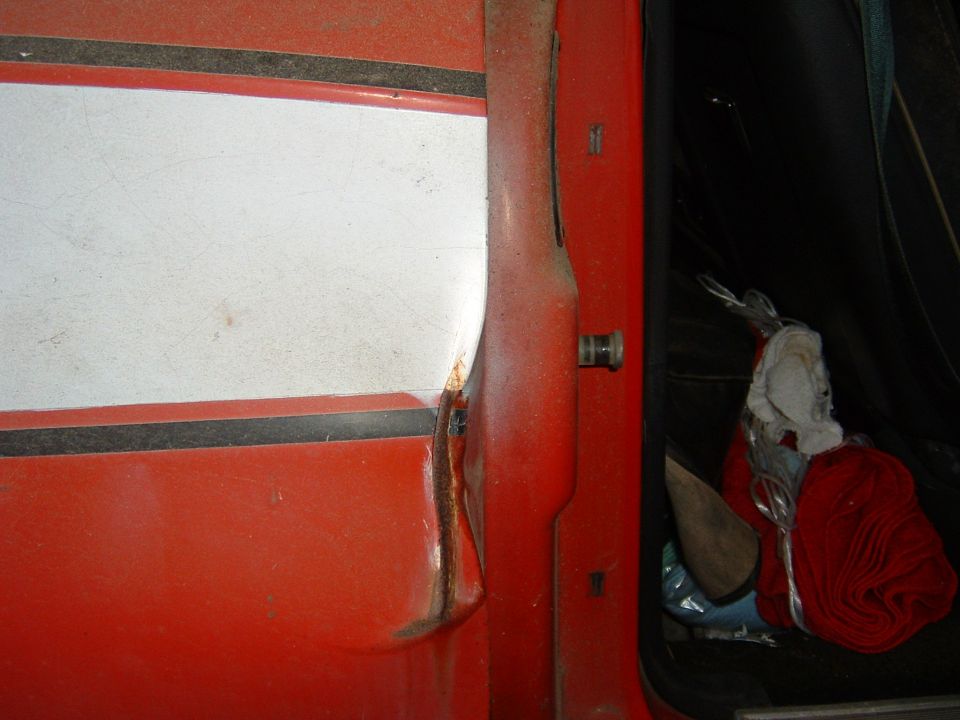 close-up of red door panel with white stripe, showing rust and interior contents