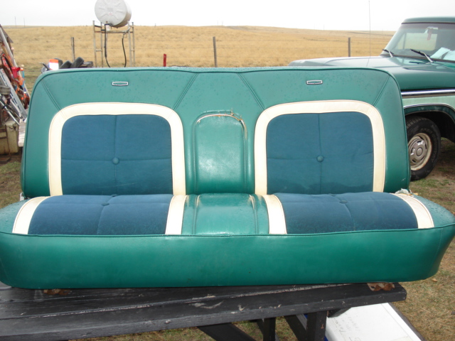 green bench seat with blue inserts and white trim, sitting on a table. Green truck in background