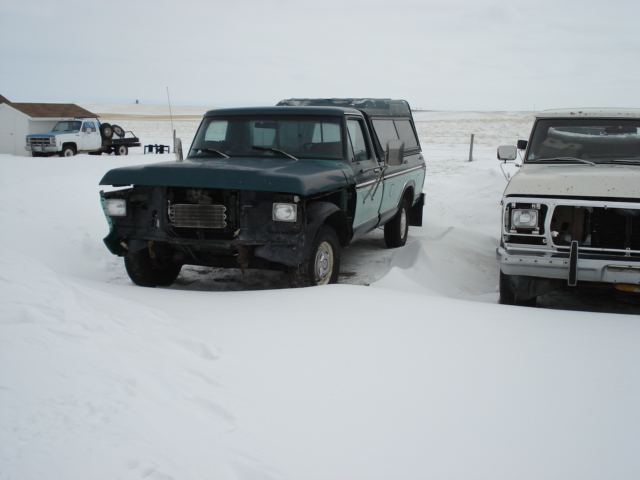 1979 Ford F-150 pickup truck with a camper shell, parked in snow next to another truck