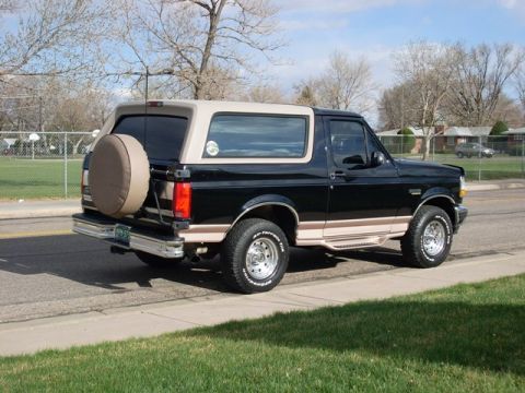 1996 Ford Bronco - This two-tone Ford Bronco is parked on a residential street with a schoolyard in the background.
