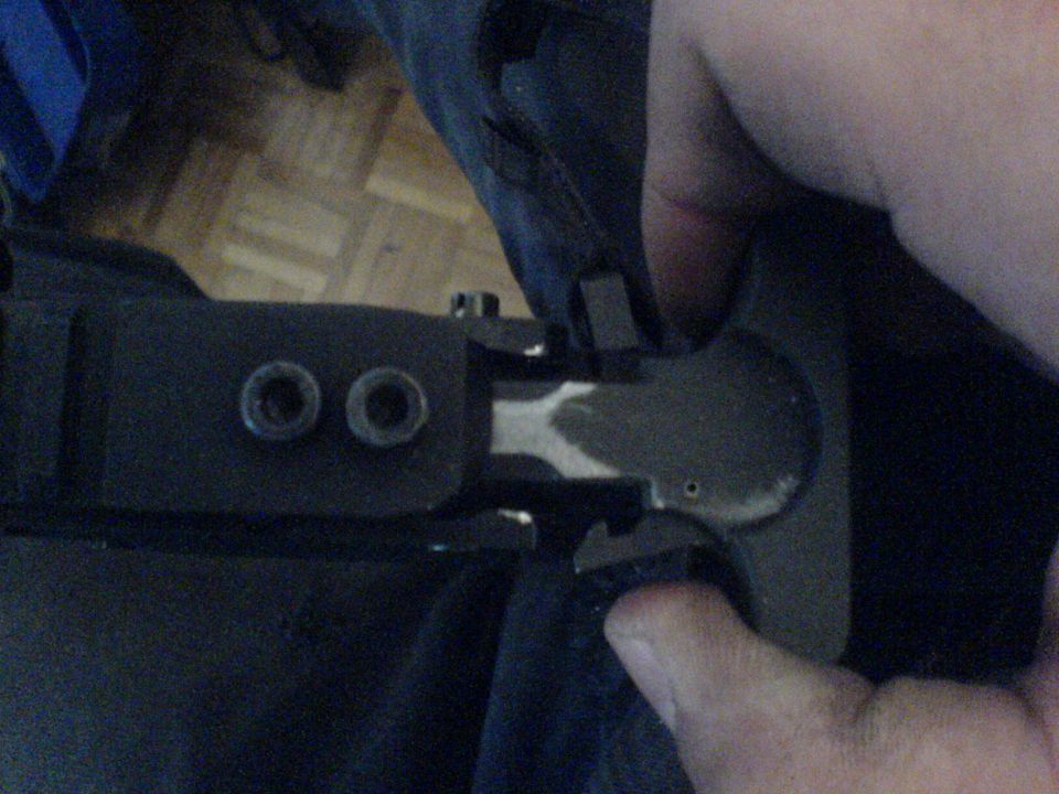 Close-up of a black metal part with two circular openings and a silver metallic component, held by a hand