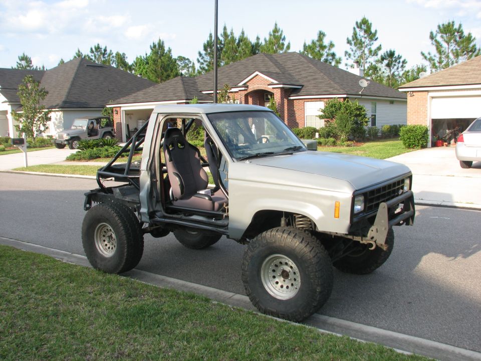 Silver modified pickup truck with roll cage, racing seats, and large tires parked on a suburban street