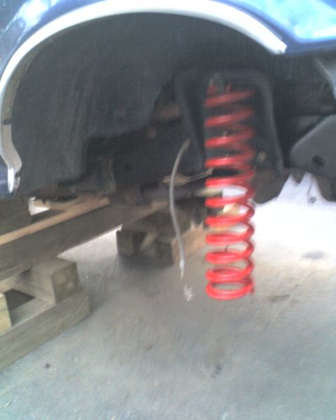 1996 Ford F-150 - A red coil spring is visible in the wheel well area of a vehicle, supported by wooden blocks.