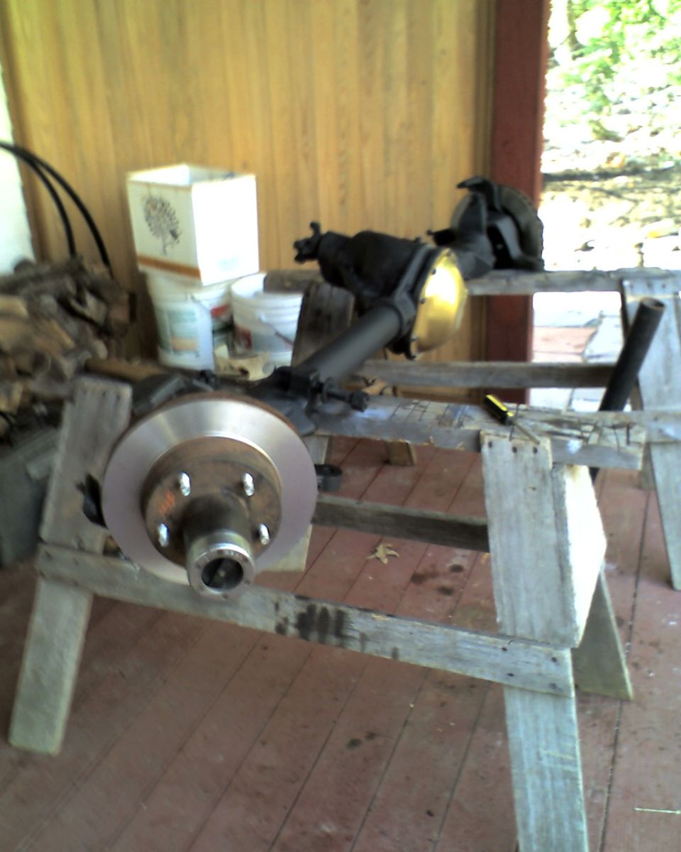 Front axle assembly with brake rotor and caliper bracket, resting on wooden sawhorses