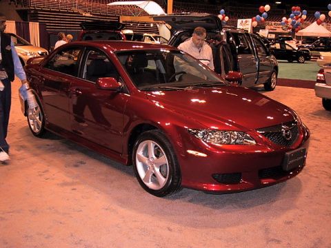 1996 Ford Taurus - A red sedan is displayed at an auto show with other vehicles in the background.
