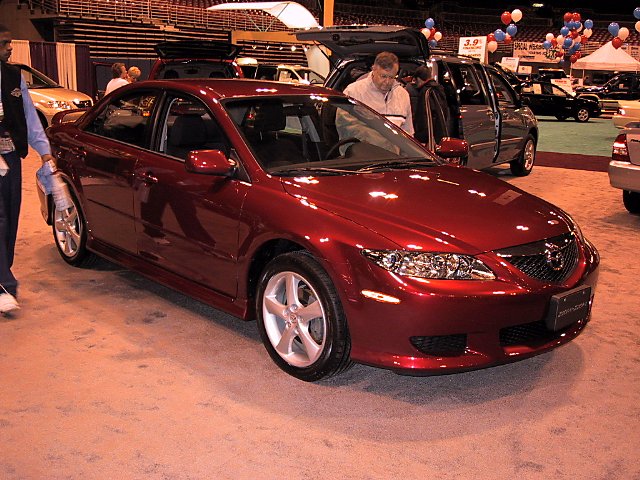 Red sedan with a man looking inside, at an auto show