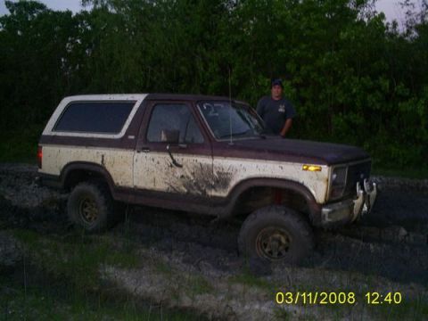1982 Ford Bronco - A muddy 1980s Ford Bronco is stuck in a dirt track with a person standing nearby.