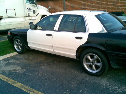 2003 Ford Crown Victoria - Side view of a two-tone black and white 2003 Ford Crown Victoria, likely a former police vehicle.