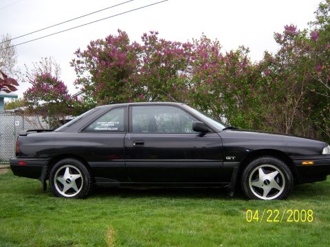 1989 Mazda MX-6 - Side profile of a black 1989 Mazda MX-6 GT coupe with distinctive star wheels.