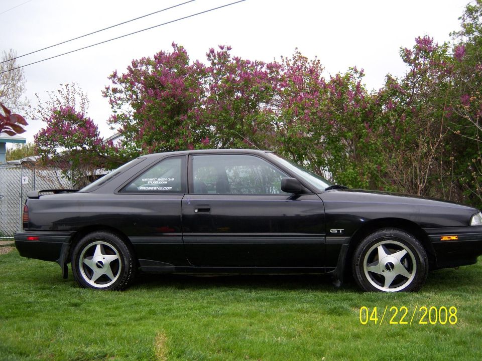 1989 Mazda MX-6 GT coupe parked on grass, side view. Sticker on rear window reads 'NORTHWEST MAZDA CLUB'