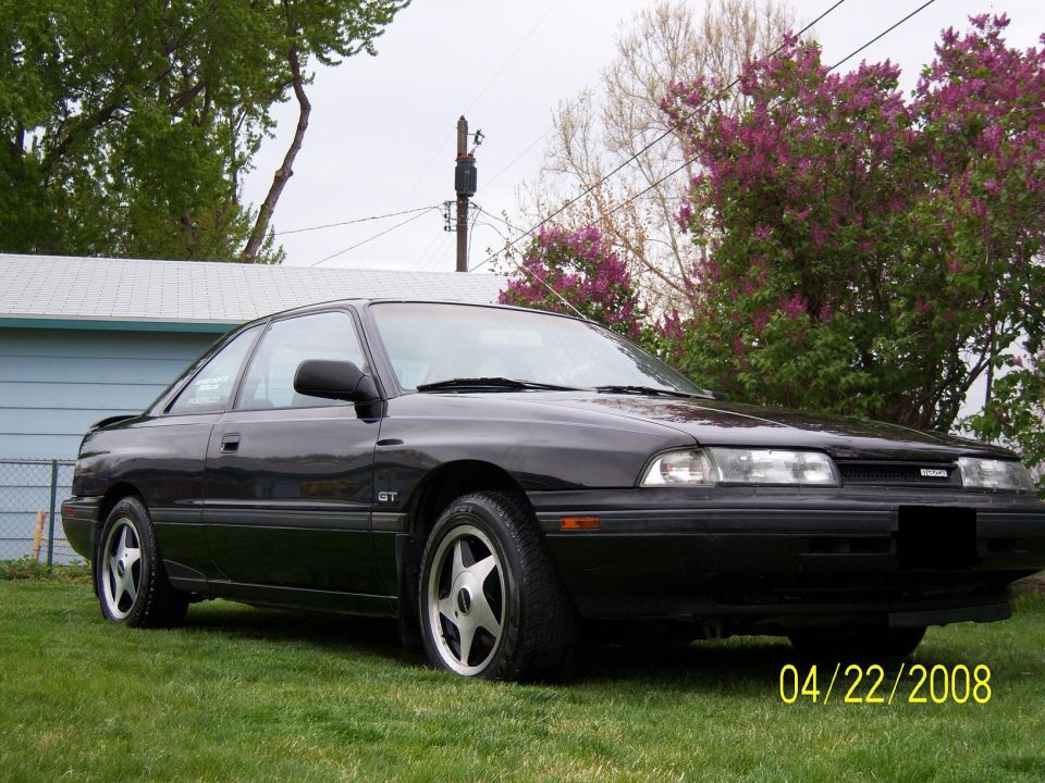 Black 1989 Mazda MX-6 GT coupe parked on grass, front 3/4 view