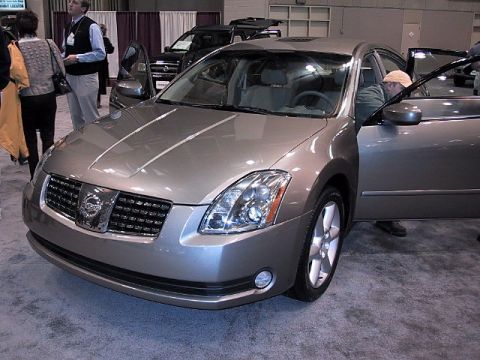 1996 Ford Taurus - A silver Nissan sedan is displayed indoors with its driver's door open, while a black SUV is visible behind it.