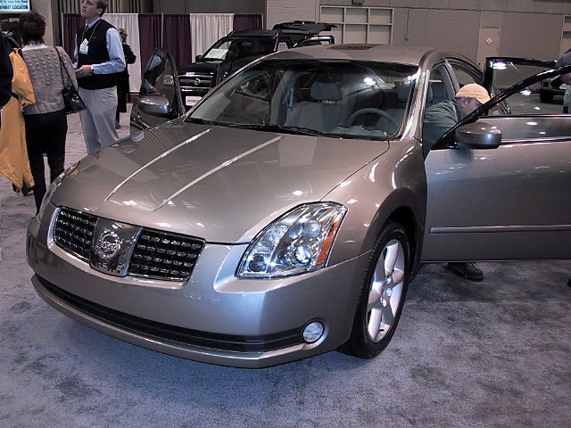 Nissan sedan with driver's door open, people nearby, and a black SUV in the background