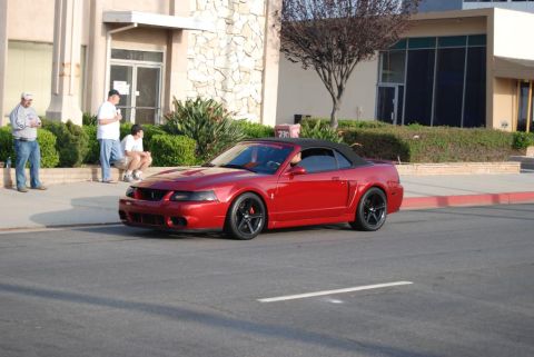 1992 Ford Crown Victoria - Red convertible sports car with black wheels and black top parked on street.