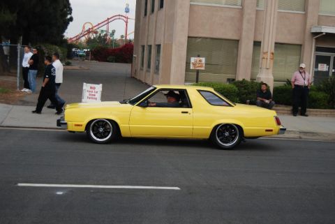 1992 Ford Crown Victoria - A yellow 1977 Ford Fairmont Futura coupe is seen from the side, modified with a lowered stance and aftermarket wheels.