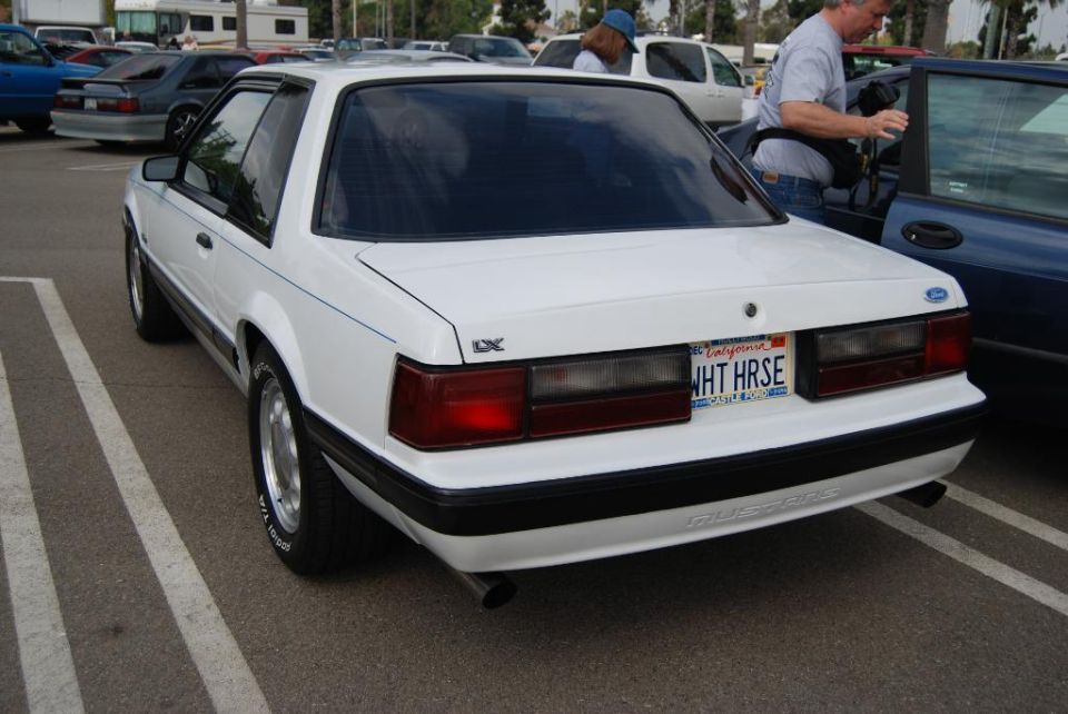 White Ford Mustang coupe parked in a lot. It has a California plate that reads WHT-HRSE