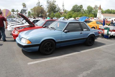 1992 Ford Crown Victoria - A blue coupe with black wheels and a '5.0' badge is parked at a car show.