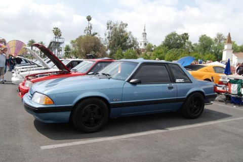 1992 Ford Crown Victoria - A line of cars are parked at an outdoor event, with a blue Ford Mustang in the foreground.