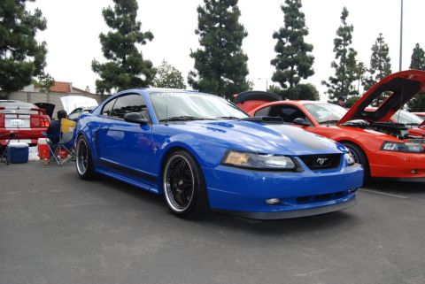 1992 Ford Crown Victoria - A blue Ford Mustang is the focus, with an orange Mustang and other vehicles visible in the background at an outdoor car show.
