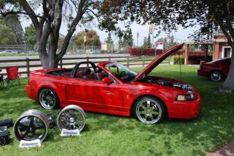 1992 Ford Crown Victoria - A red convertible sports car is displayed with its hood open, alongside spare wheels, with another vehicle visible in the background.