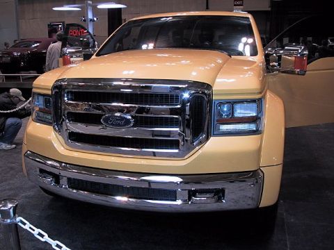 1996 Ford Taurus - A yellow Ford F-Series truck is displayed at an auto show, with a red car visible in the background.