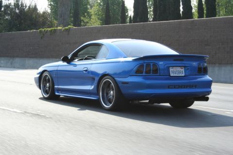 1992 Ford Crown Victoria - Rear view of a blue 1996 Ford Mustang Cobra driving on a highway.