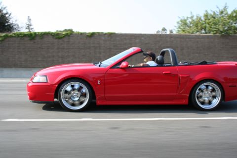 1992 Ford Crown Victoria - A red convertible Mustang is captured in a side profile shot while driving on a highway.