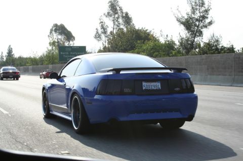1992 Ford Crown Victoria - A blue Ford Mustang drives down the highway with other vehicles visible.