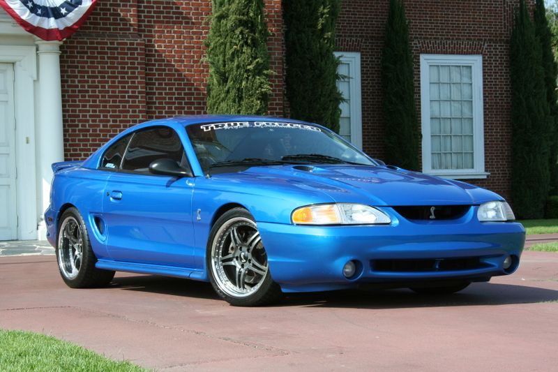 Blue coupe with a cobra emblem on the grille and a banner on the windshield