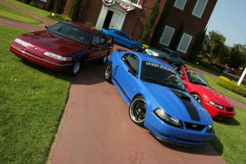 1992 Ford Crown Victoria - Several Ford vehicles are parked outside a building, including a maroon Crown Victoria and multiple Mustangs.
