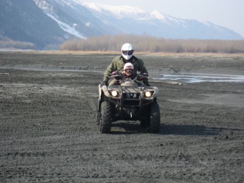 1990 Ford F-250 - Two individuals ride an all-terrain vehicle across a muddy plain with mountains in the background.