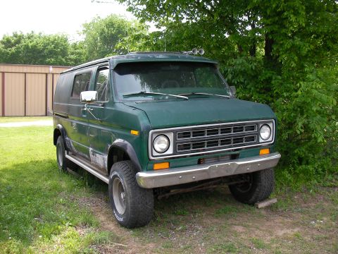 1978 Ford E250 - A green van with off-road tires and a chrome bumper is parked on a grassy area near trees.