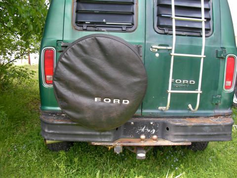 1978 Ford E250 - The rear of a green van shows a spare tire cover and a ladder attached to the back doors.