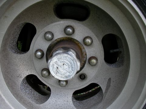 1978 Ford E250 - A close-up view of a vehicle's wheel hubcap, showing lug nuts and a central cap with some writing.