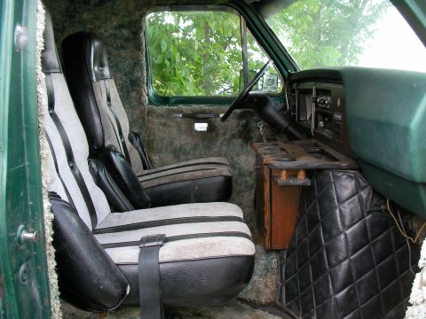1978 Ford E250 - The interior of a van shows two front seats, a dashboard, and a custom wooden console with cup holders.