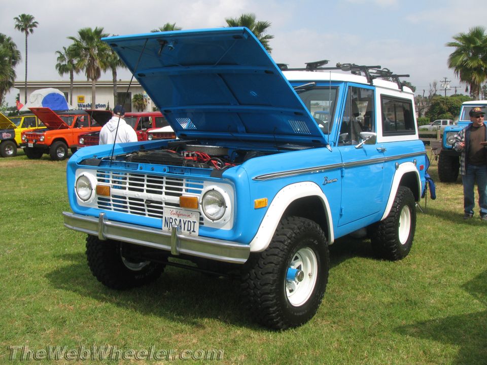 Blue 1970 Ford Bronco with white top and fender flares, hood open, parked on grass