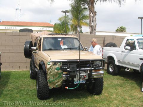 1968 Ford Mustang - A modified tan Ford Bronco II is parked on grass next to a white pickup truck, displaying its off-road features.