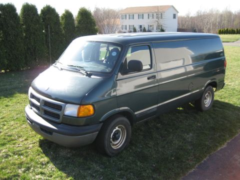 1994 Ford Bronco - A dark green cargo van is parked on a grassy lawn in front of a house and trees.