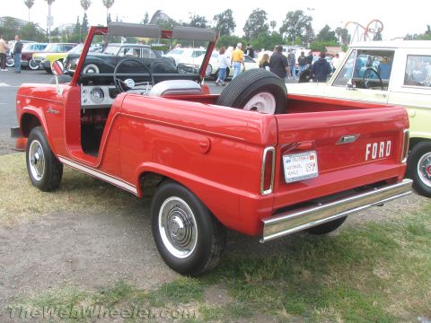 1968 Ford Mustang - A red Ford Bronco is parked outdoors with other vehicles and people in the background.